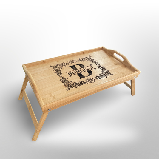 A bamboo serving tray with folding legs with a custom logo engraved onto the center of the serving tray